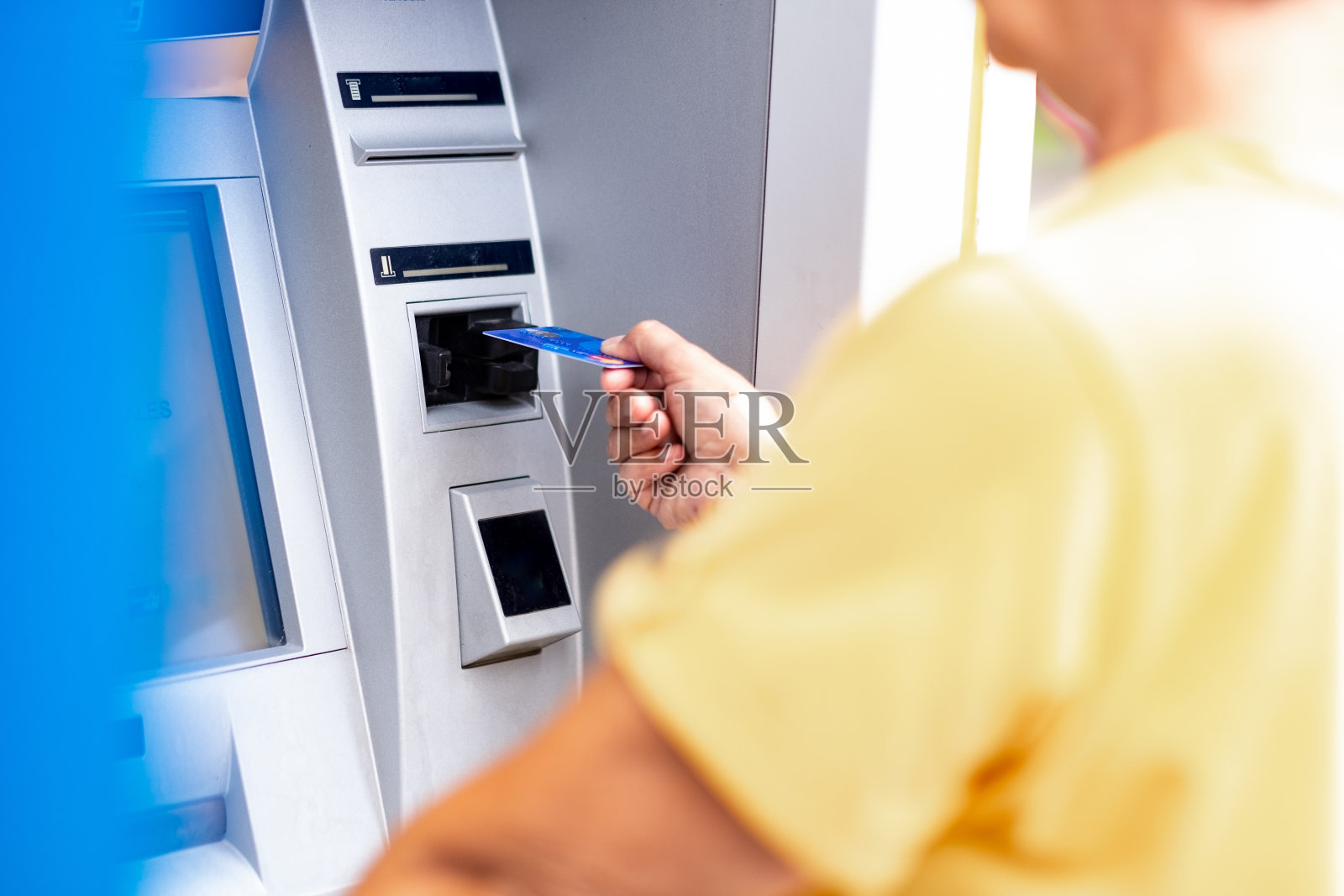一个黄衣服的女人正在自动取款机上从信用卡里取钱照片摄影图片