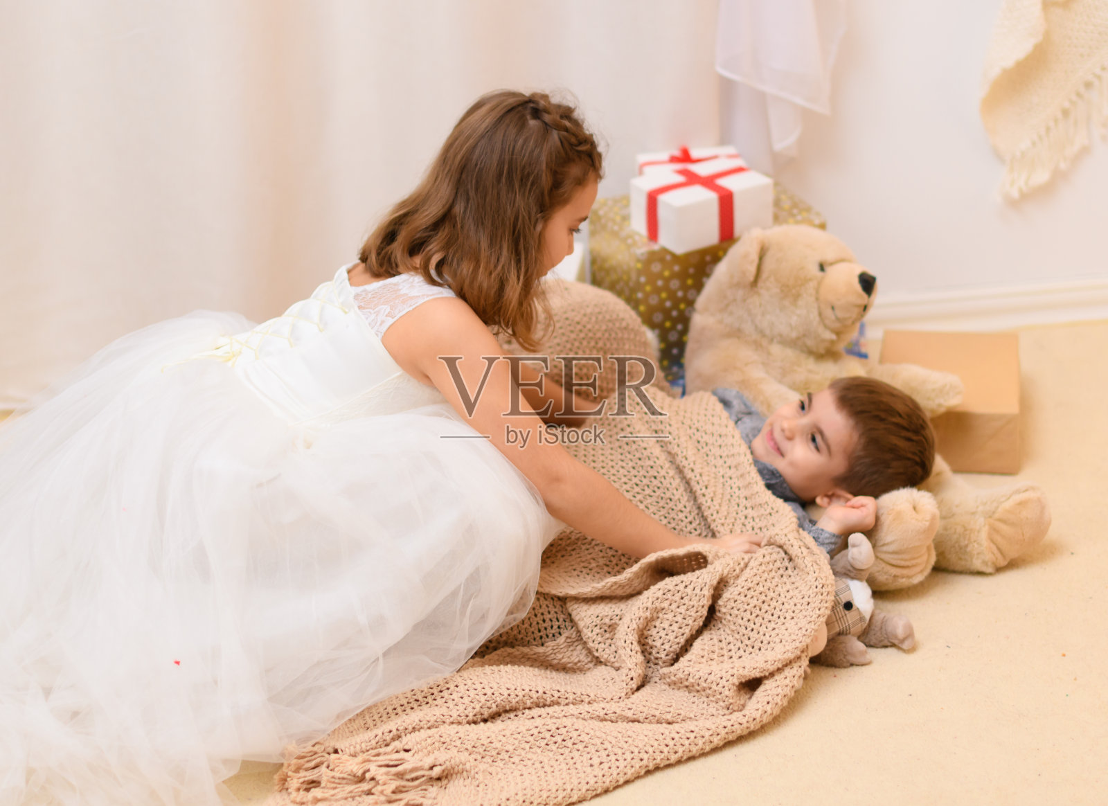 男孩躺在地板上，女孩给他盖上毯子，家里装饰着节日灯和礼物照片摄影图片