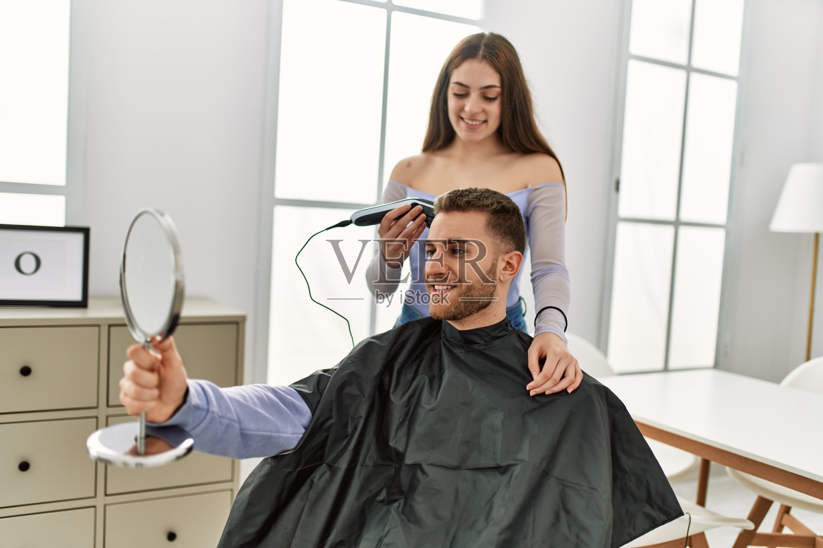 一个年轻女子在家给她男朋友剪头发。照片摄影图片