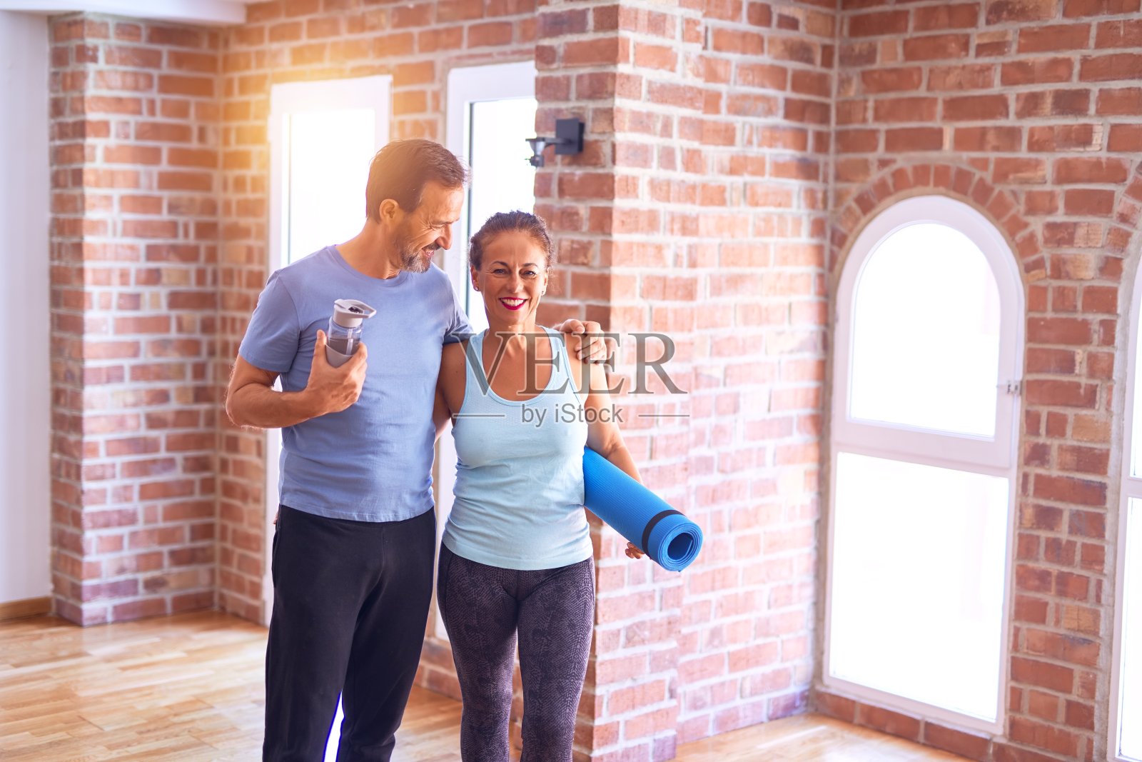 中年漂亮运动夫妇微笑幸福。在健身房面带微笑的站着，抱着垫子照片摄影图片