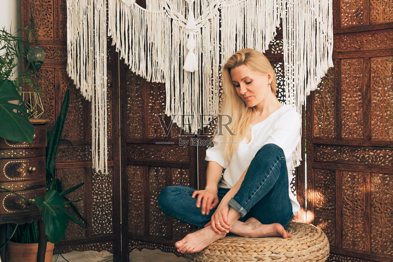 一个年轻迷人的金发女人在一个装饰着流苏装饰的木制图案屏幕前摆姿势。手工制作的概念。家居装饰照片摄影图片