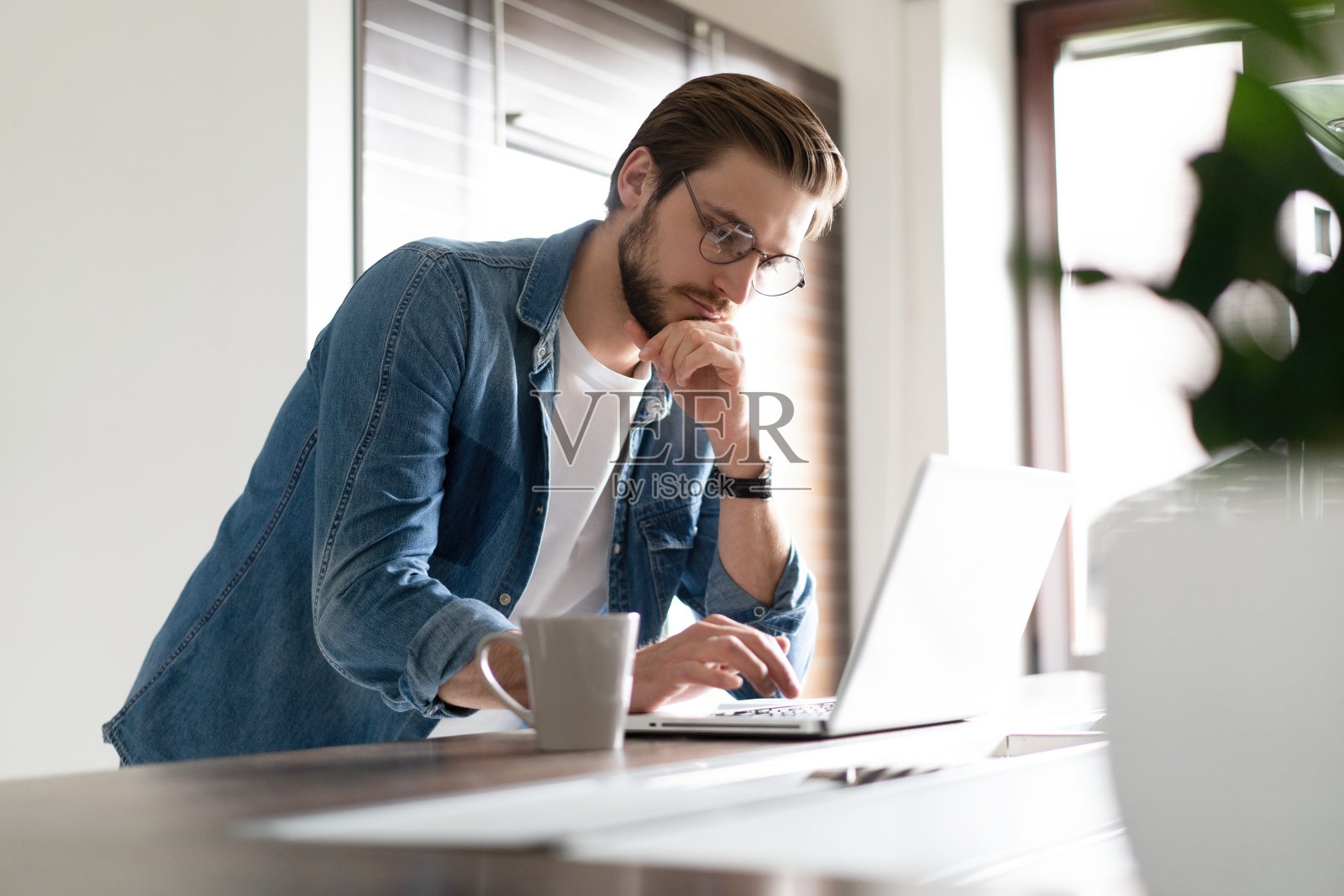 年轻人随便上网用笔记本电脑工作，站在厨房桌子旁边，看着电脑屏幕照片摄影图片