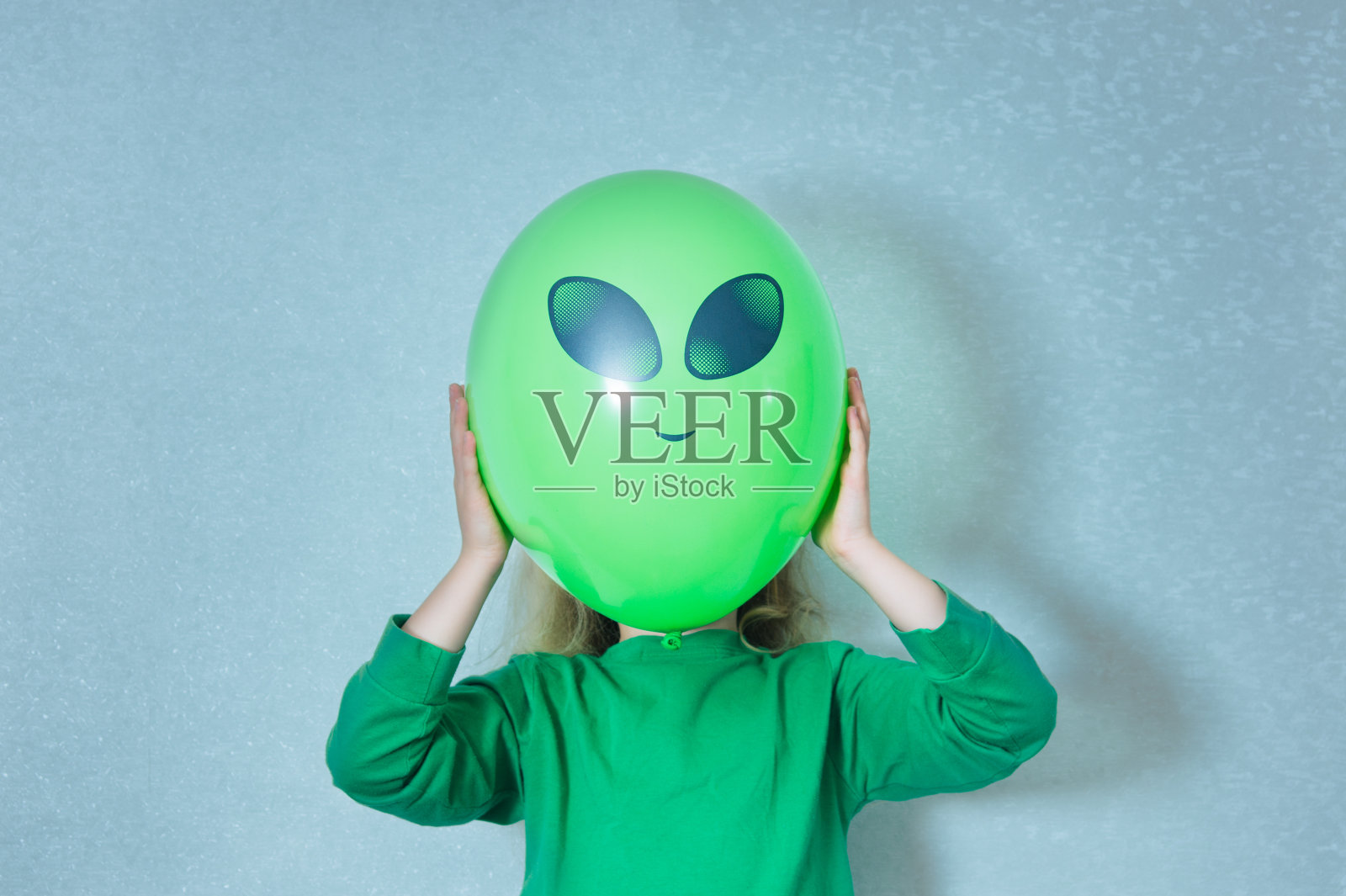 孩子穿着绿色衣服玩外星人。带着一个绿色球的女孩，画着眼睛和脸照片摄影图片