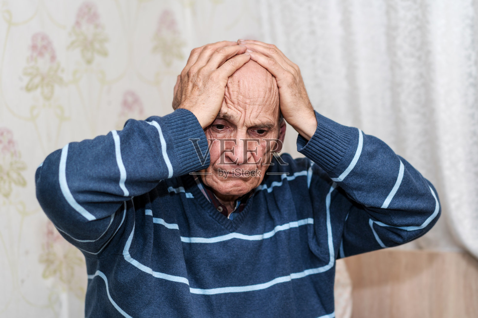 头痛的老人双手抱着头坐在床上。照片摄影图片