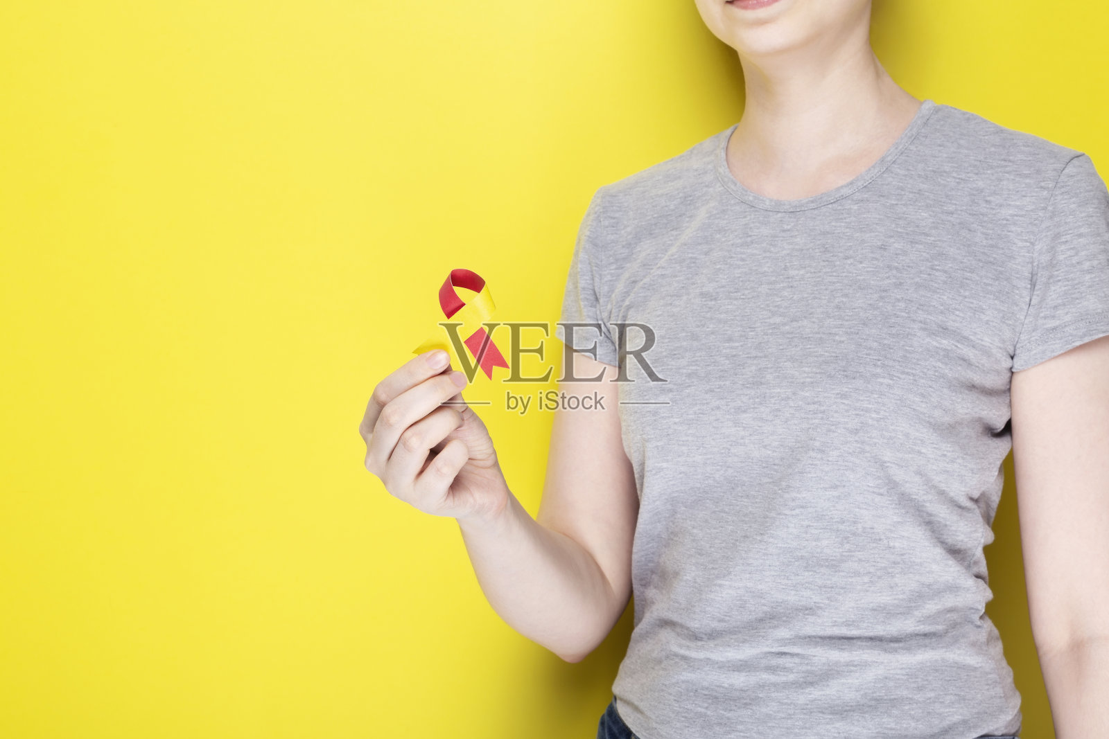 世界肝炎日的概念。身穿灰色t恤的女孩手中拿着象征意识的红黄丝带。黄色背景。本空间照片摄影图片