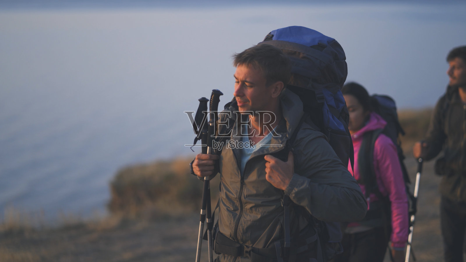 游客们背着背包在海边的山景上行走照片摄影图片