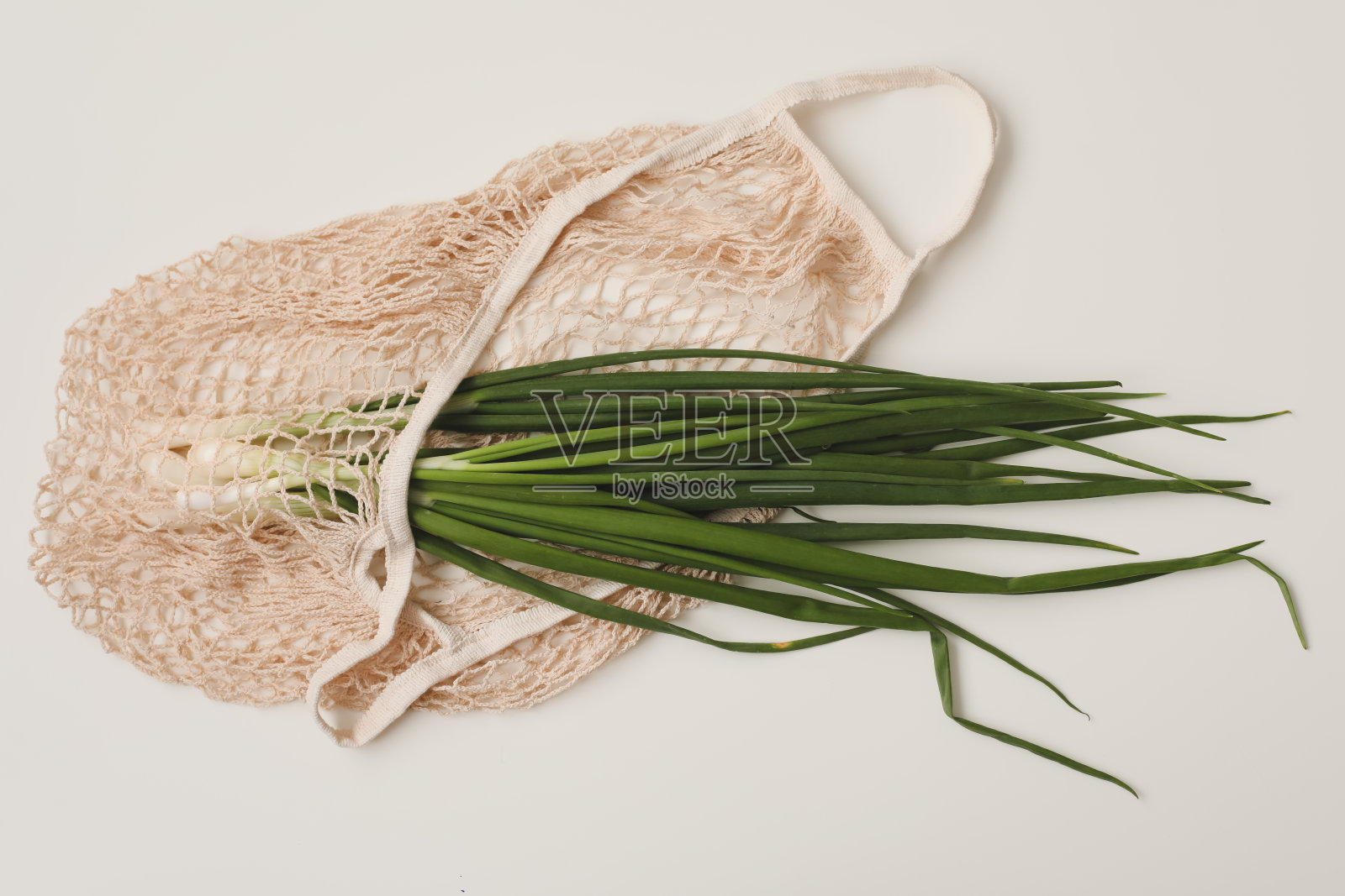 新鲜的绿洋葱在环保袋白色背景俯视图，平铺。健康的有机食品照片摄影图片