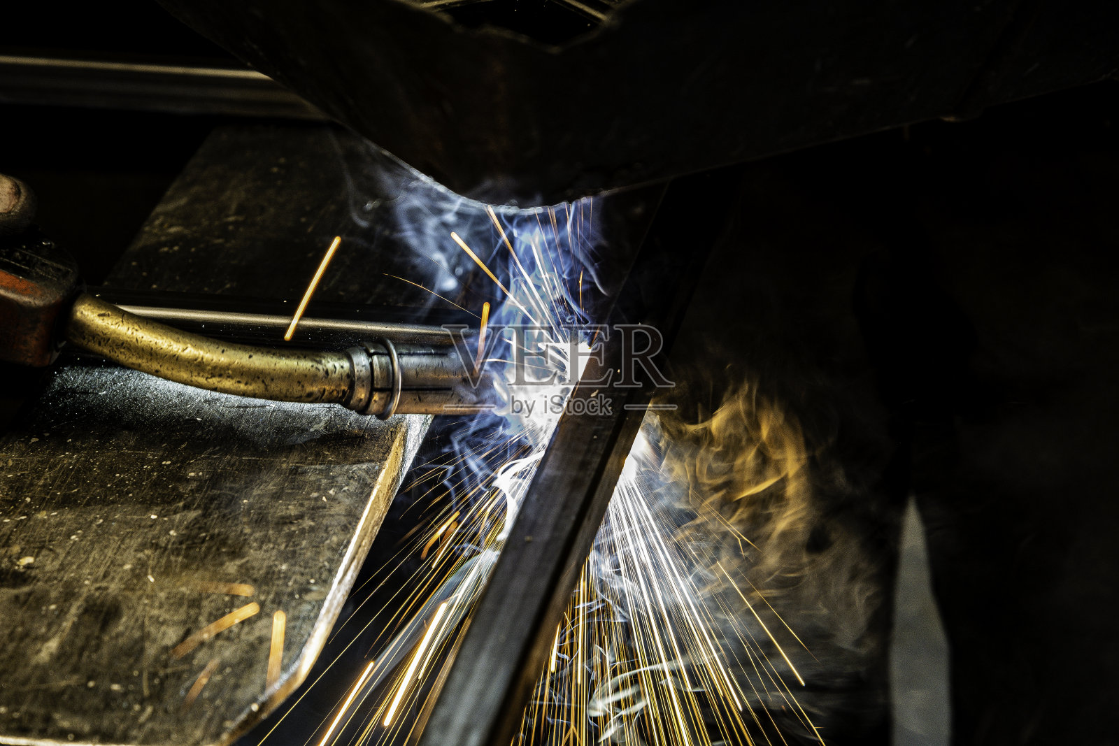 一个工人焊接两方钢管的特写。你可以看到管子和来自焊料的烟以及焊料热在金属上产生的强烈的白色和蓝色光。照片摄影图片