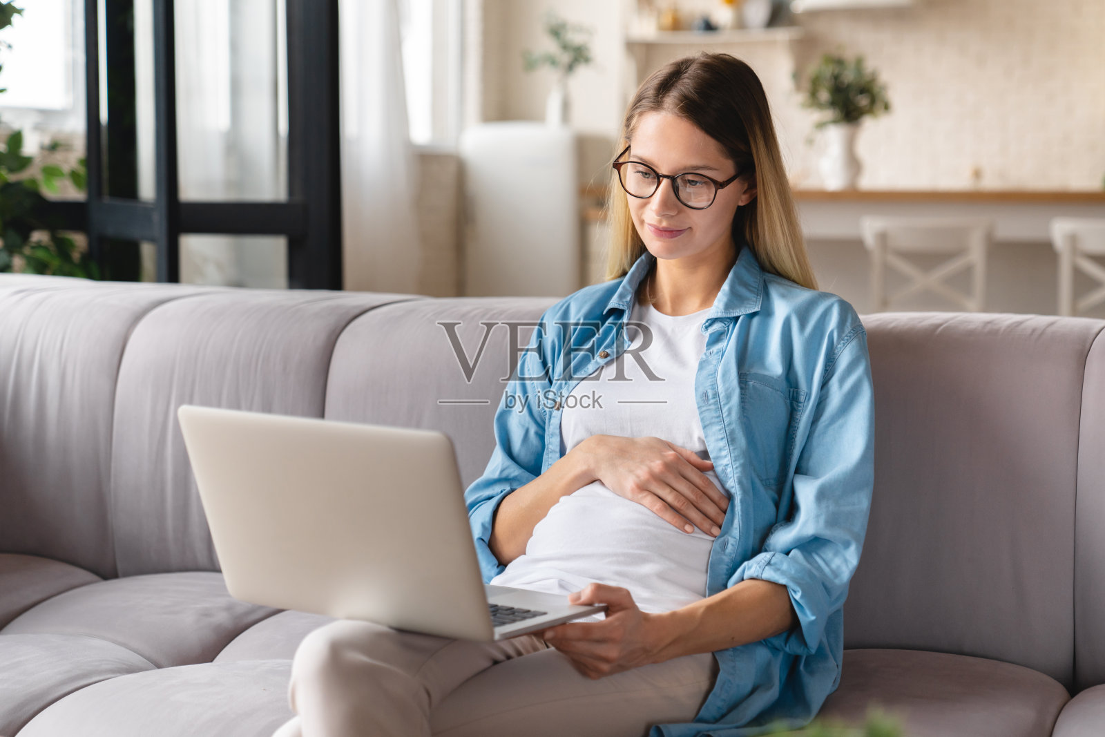 年轻的白人孕妇坐在沙发上用笔记本电脑。孩子的期望。搜索浏览信息和产假。社会距离的概念照片摄影图片