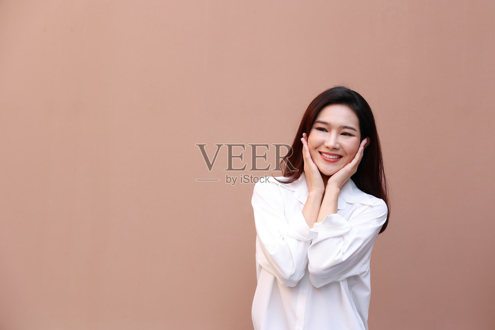 一个美丽的亚洲女人的肖像与健康的皮肤。她穿着一件白色毛衣。她高兴地笑了。冬季保健理念。孤立在棕色背景上照片摄影图片