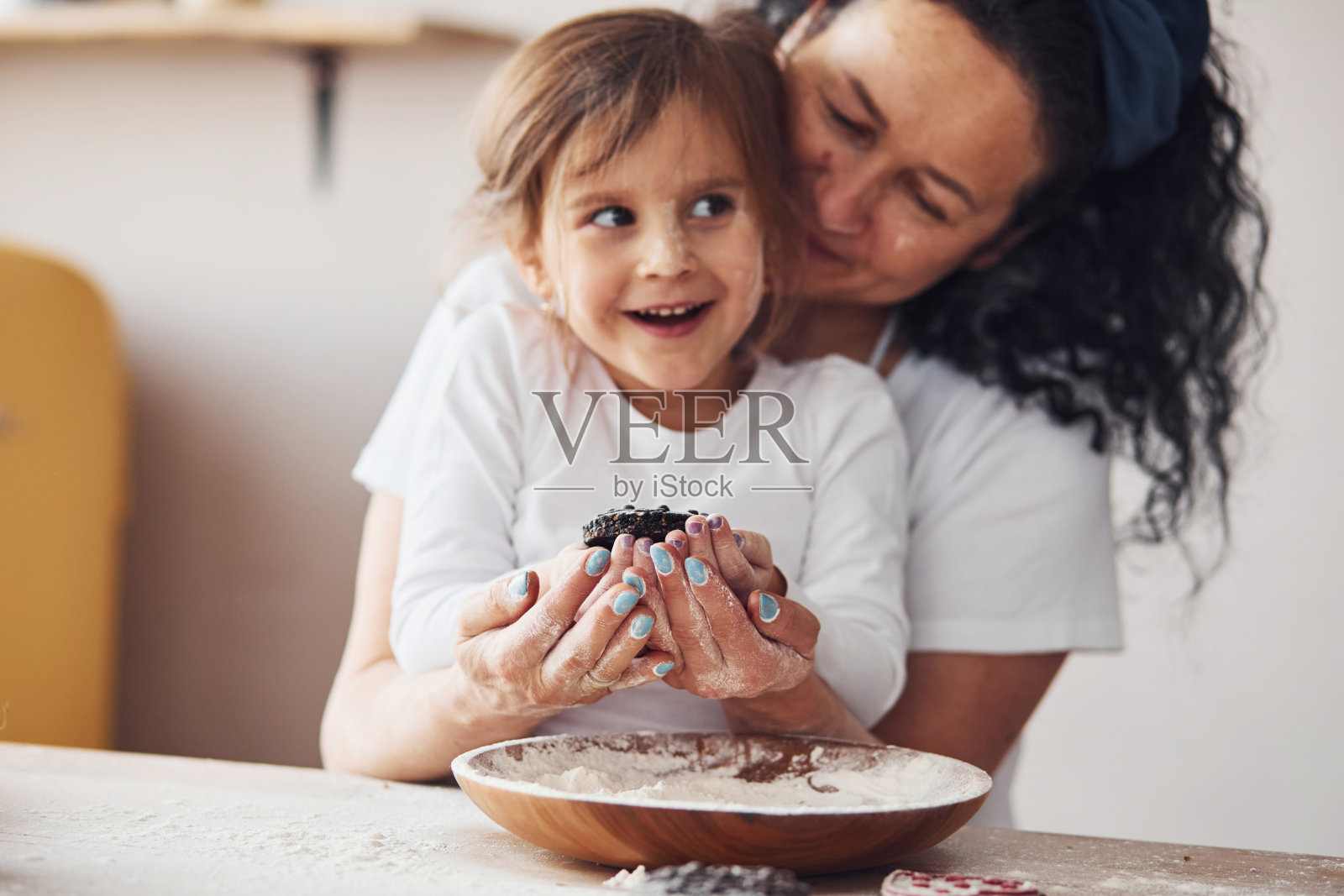 年长的妇女和她的孙女手里拿着新鲜的甜饼干在厨房里，面粉在盘子里放在桌子上照片摄影图片