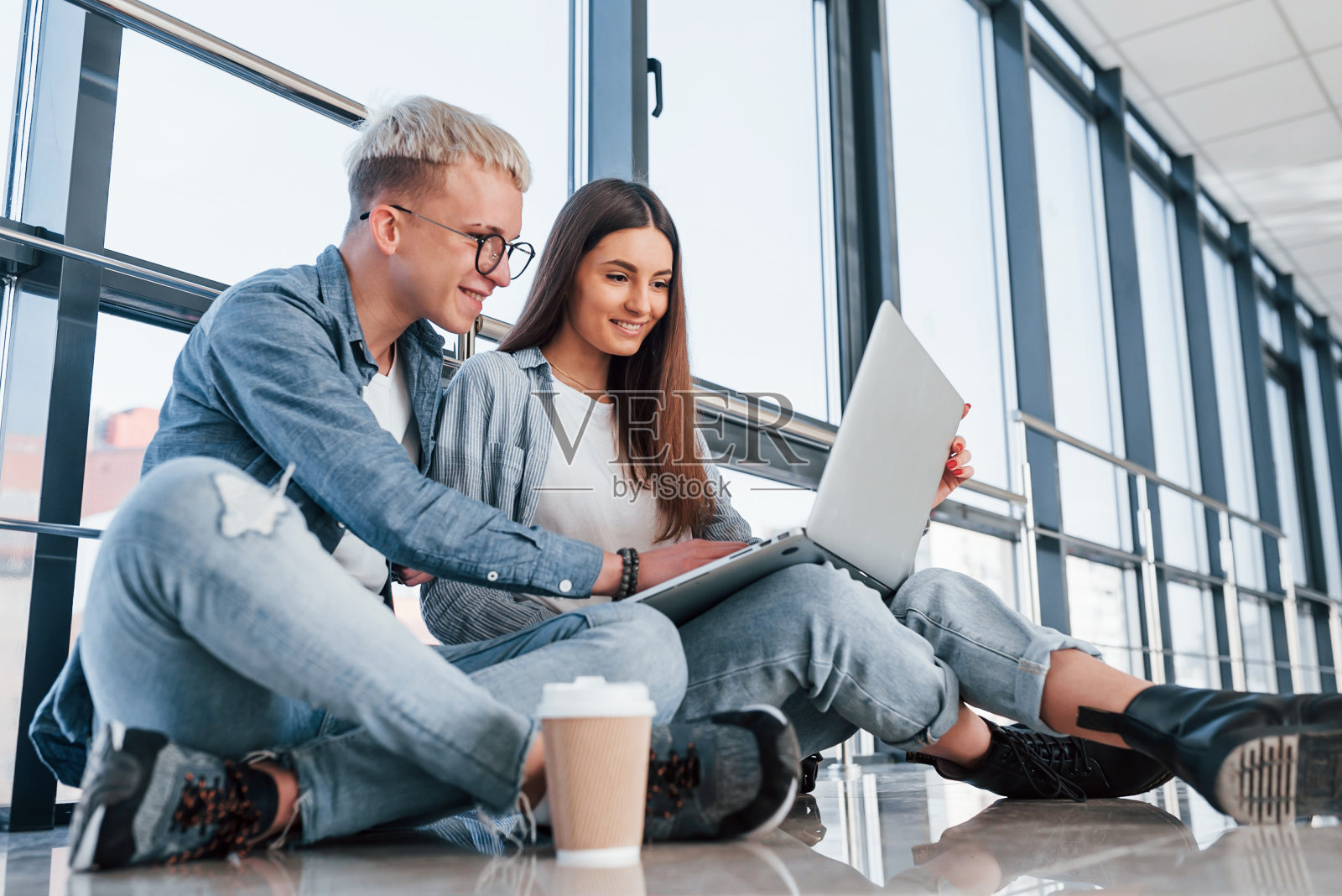 年轻的男女学生一起坐在地板上，拿着笔记本电脑照片摄影图片
