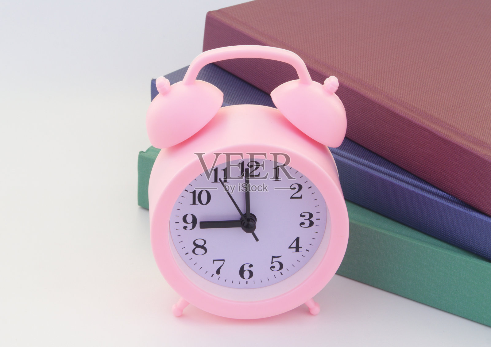 粉红色的闹钟和堆叠不同的书与文字的空间。照片摄影图片