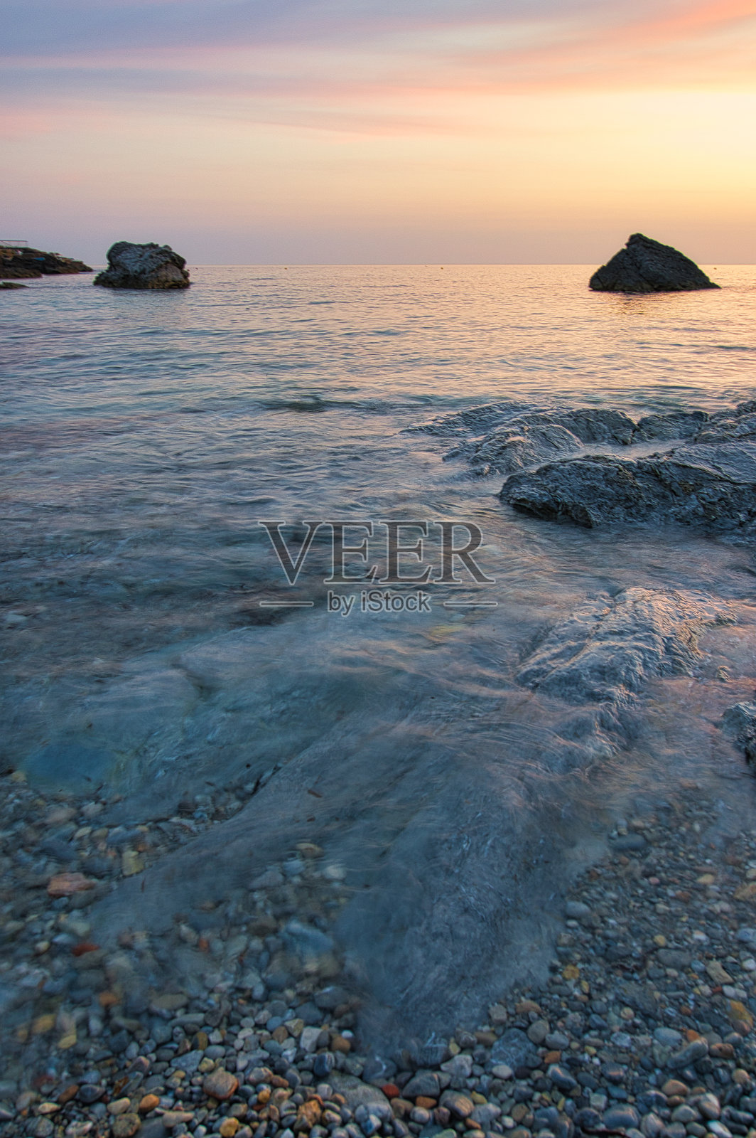 美丽的垂直海景日落从卵石海岸在海上日落。照片摄影图片