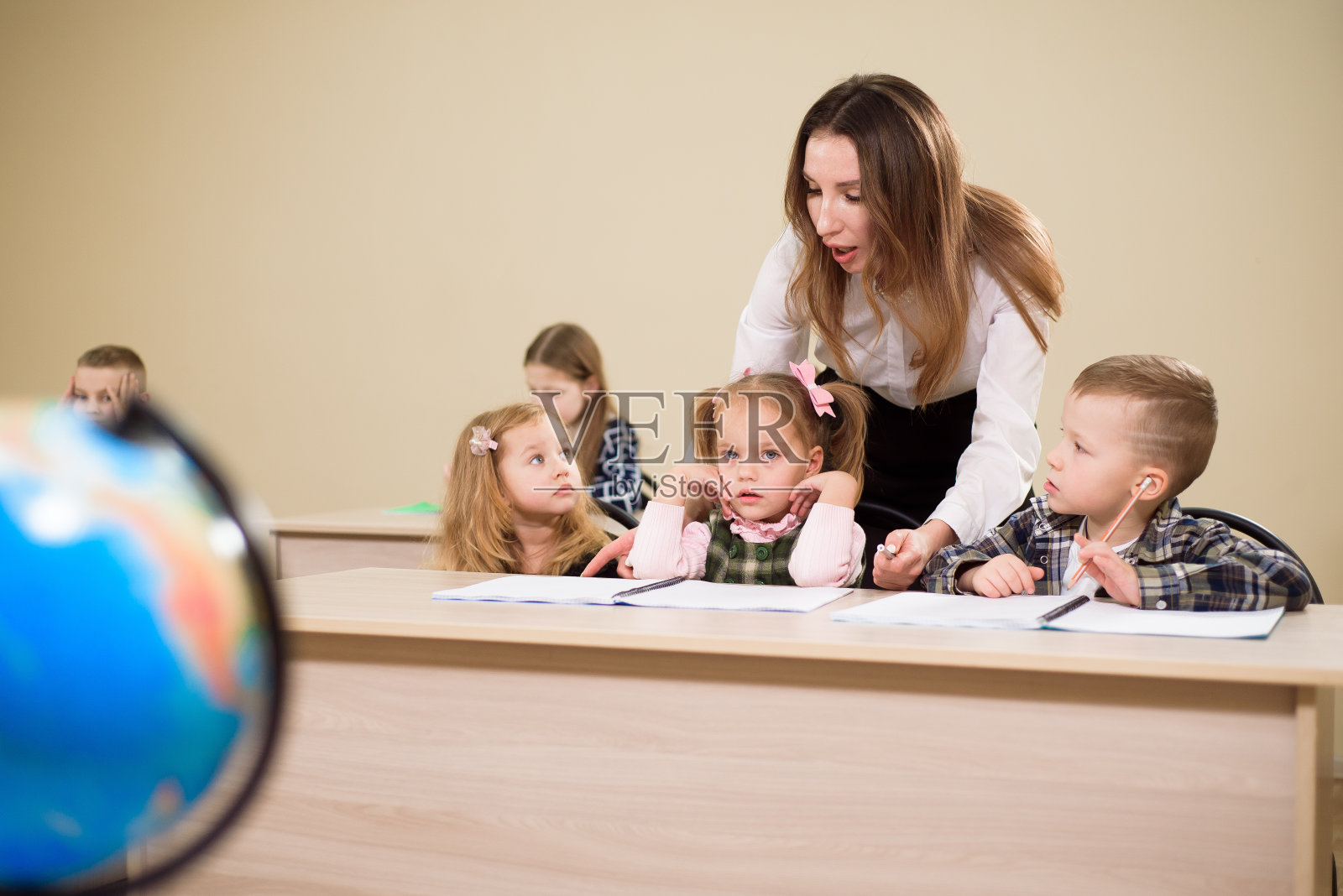 小学老师帮助一个女孩在她的桌子上写作。照片摄影图片