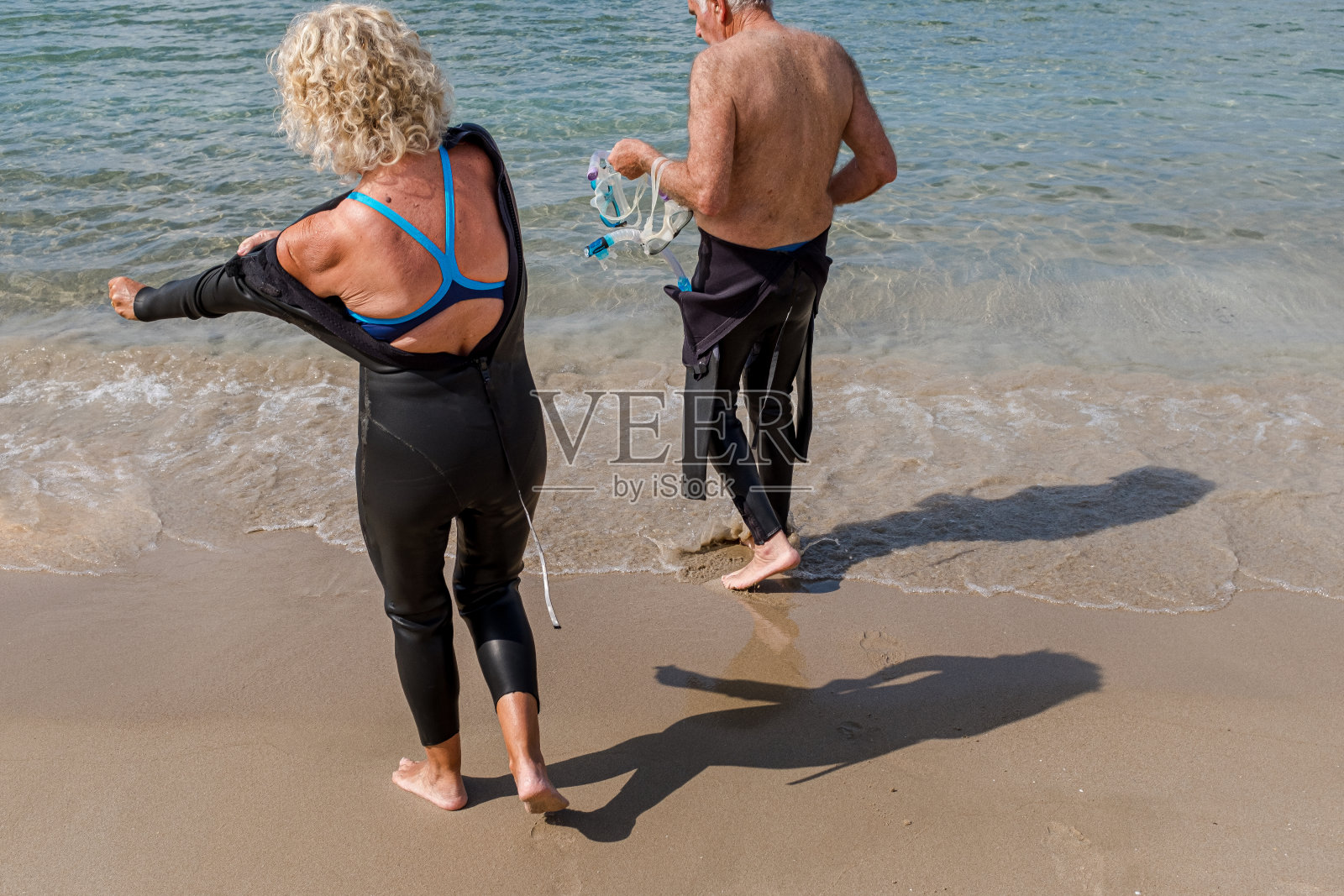 一对退休夫妇穿着潜水服在海滩上游泳。照片摄影图片