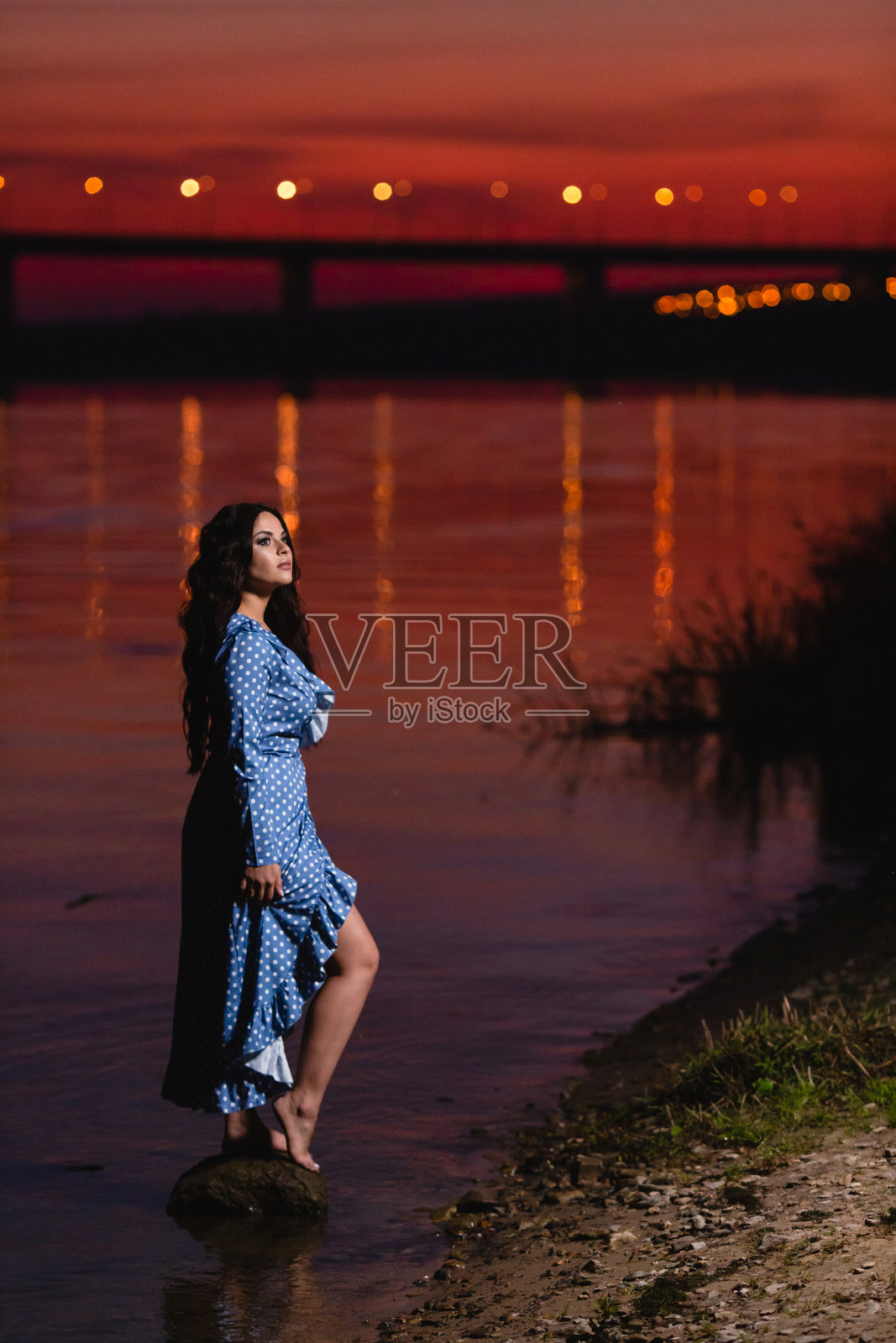 美丽的年轻姑娘，一头乌黑的长卷发，站在河边照片摄影图片