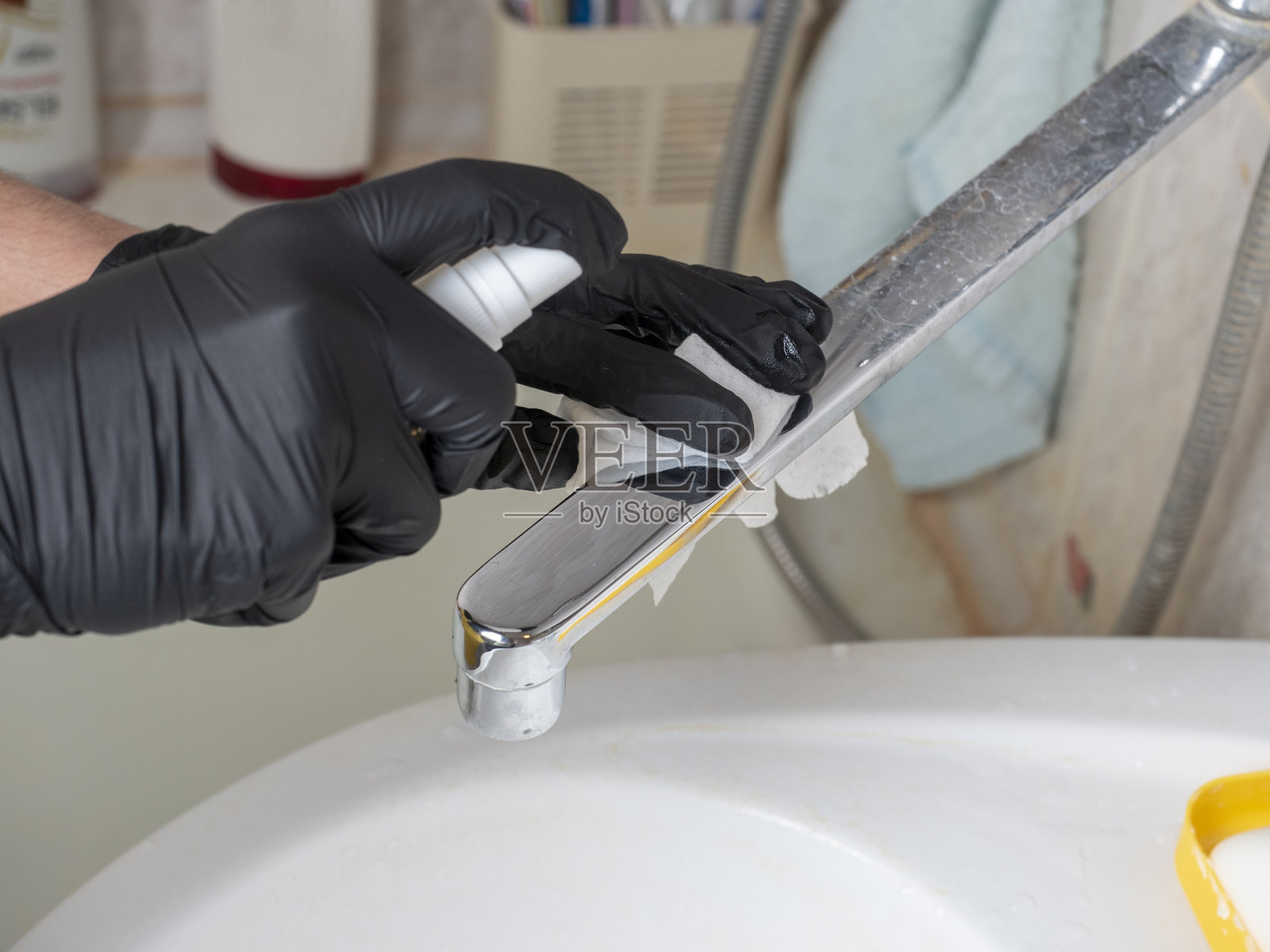 一个戴着黑手套的男人在屋里摆弄水龙头。它可以喷洒并用一块布清洗。浴室及家居清洁照片摄影图片