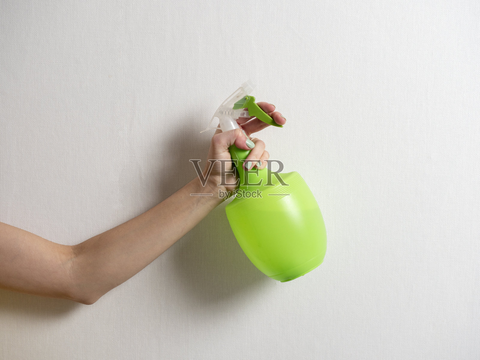 一个女人的手里拿着一个塑料瓶子，灰色的背景上有一个绿色的喷雾器。家居护理和清洁的概念。照片摄影图片