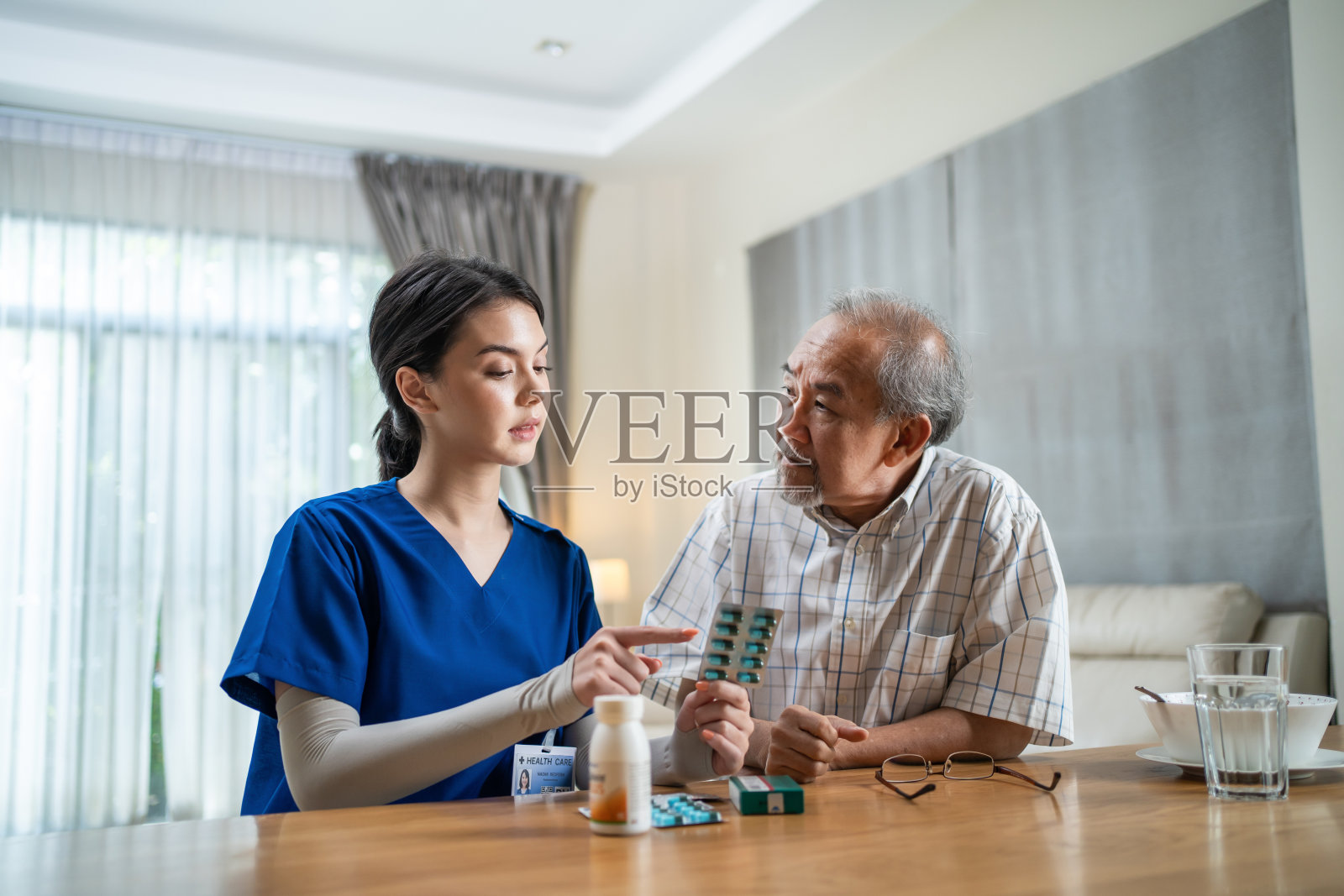 亚洲老年男性患者在养老院向医生护士咨询。护理治疗师药剂师女孩拿着药瓶，向家里的老残疾人解释处方照片摄影图片