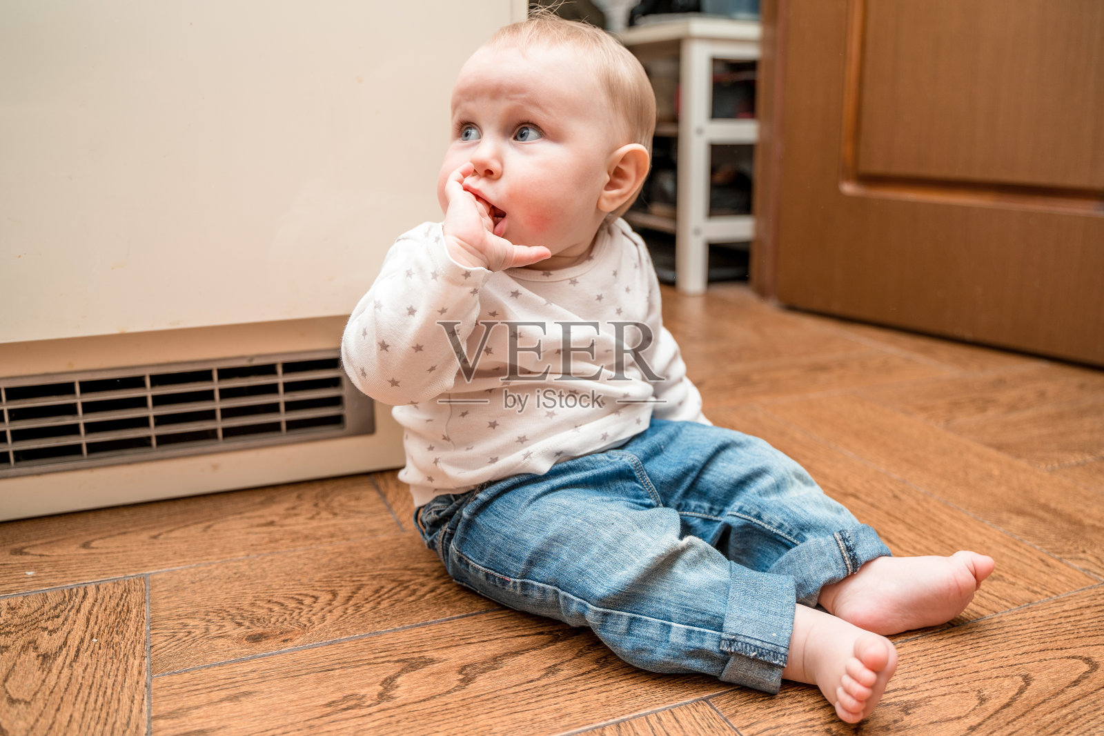 可爱的婴儿坐在房子的地板上，看着别处照片摄影图片