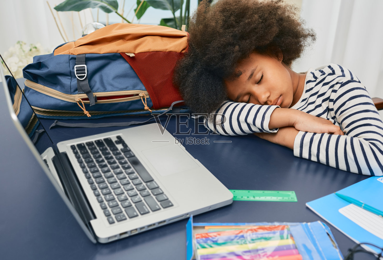 一个小女生在家在线学习的时候睡着了，在一节艰难的课后把她卷曲的头放在学校的桌子上，然后休息照片摄影图片