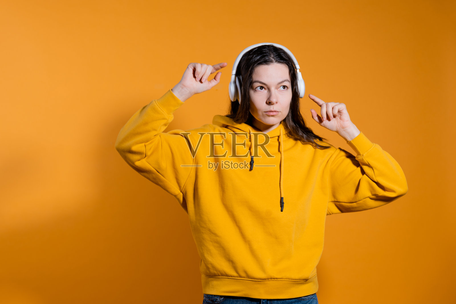 音乐爱好者喜欢音乐。一个穿着黄色帽衫戴着白色无线耳机的年轻女子，照片摄影图片