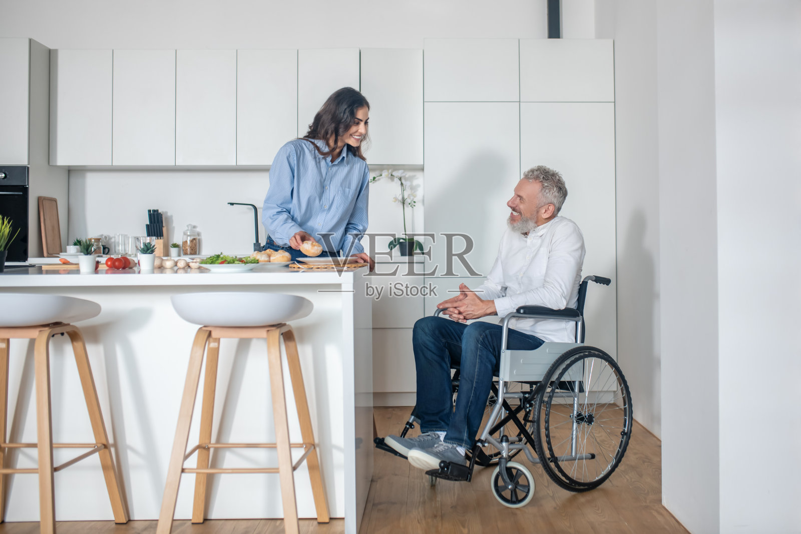 一个年轻女人在做早餐，她残疾的丈夫坐在旁边照片摄影图片