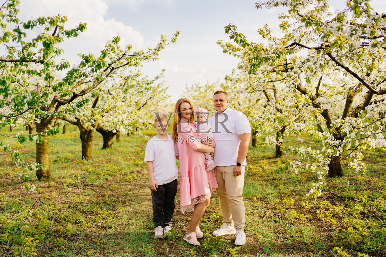 一家人带着儿女在春天的花圃里。婴儿唇裂。照片摄影图片