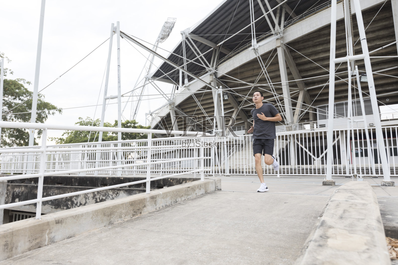 年轻的亚洲运动员在体育场前跑步。这个人在户外训练。照片摄影图片