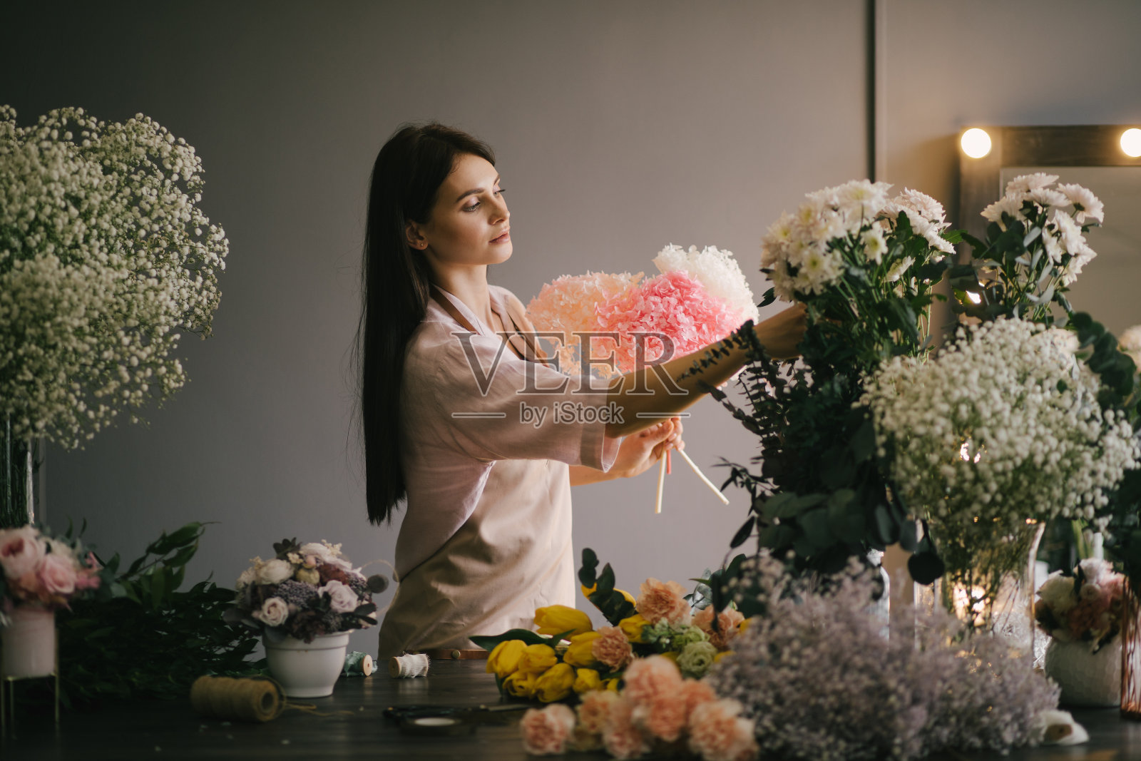 年轻女子花匠在她的花室工作，用新鲜的植物和鲜花制作美丽的花束。照片摄影图片