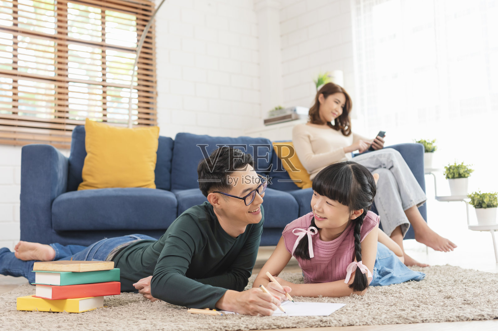 放松亚洲母亲在沙发上看书，父亲和女儿在客厅绘画艺术在家里。照片摄影图片