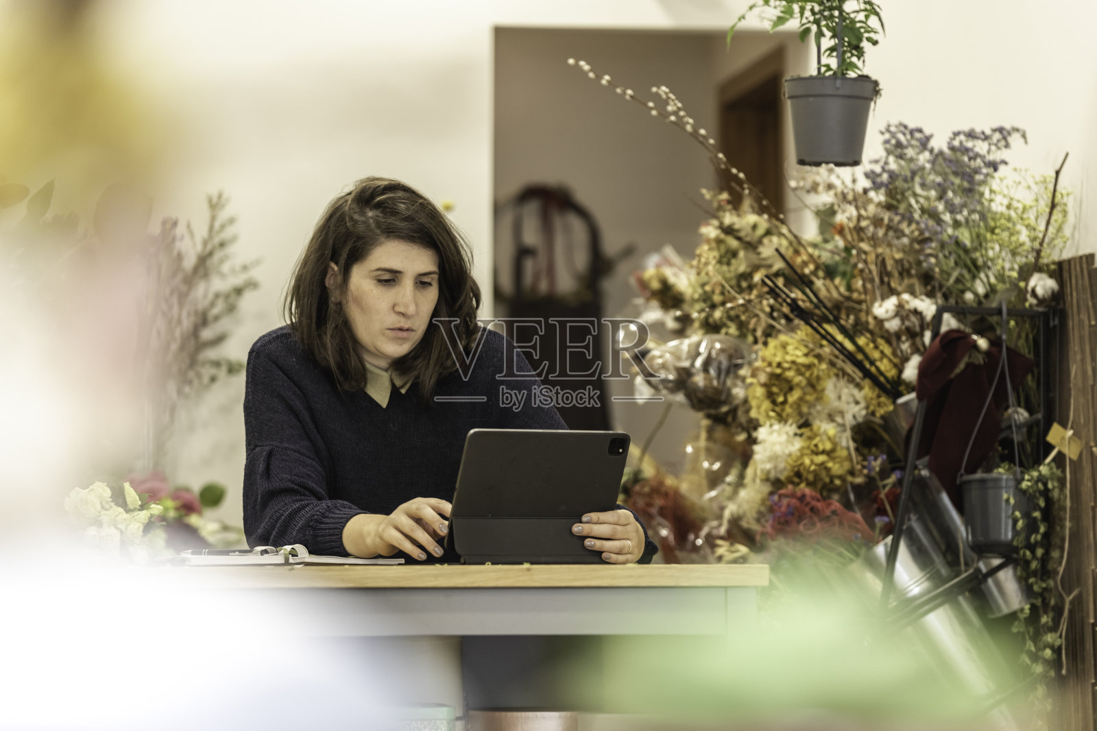一个开朗的年轻女子在花店工作，在一台小笔记本电脑前安排会议议程，女商人的概念。照片摄影图片