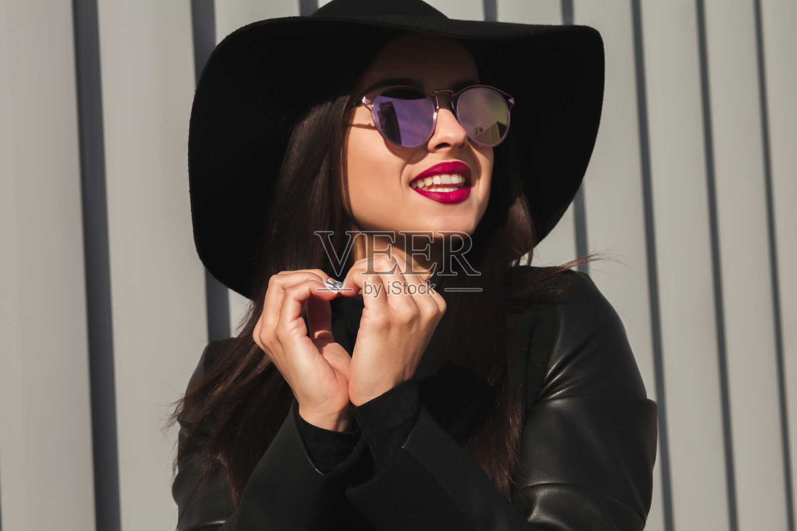 快乐的年轻模特戴着时尚的眼镜和帽子，用手做心形标志在街上照片摄影图片