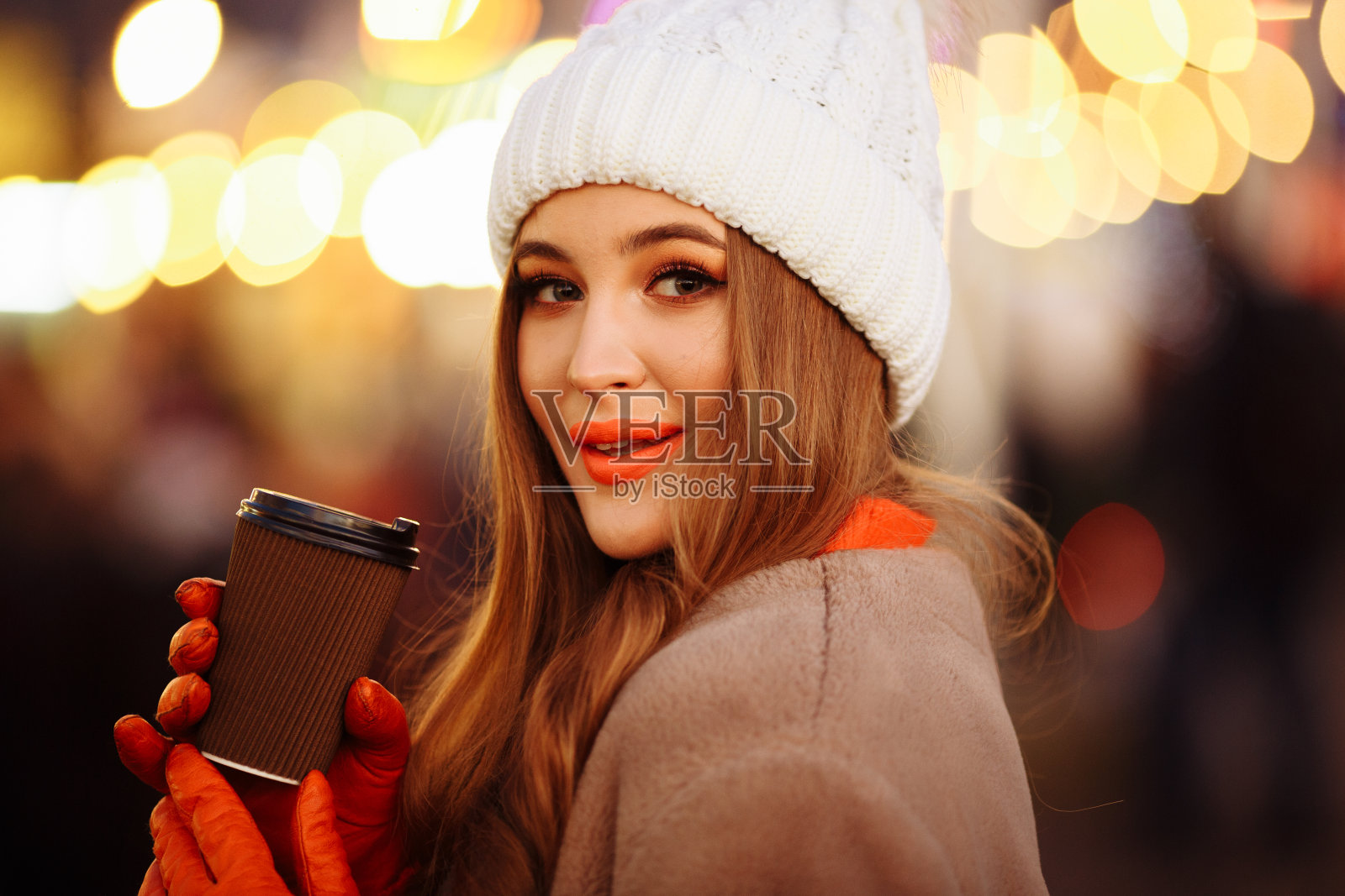 美丽的女孩在灯光的背景下喝着咖啡，在大街上，过节，新年。漫步在夜城照片摄影图片