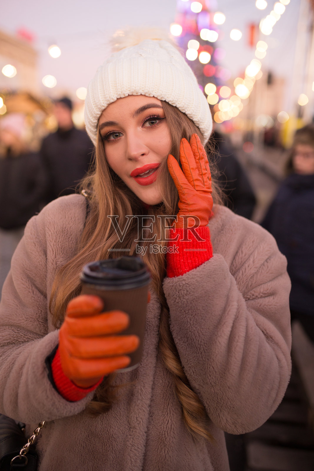 美丽的女孩在灯光背景下喝着咖啡，在街上，假期，新年。在黄昏的城市里散步照片摄影图片
