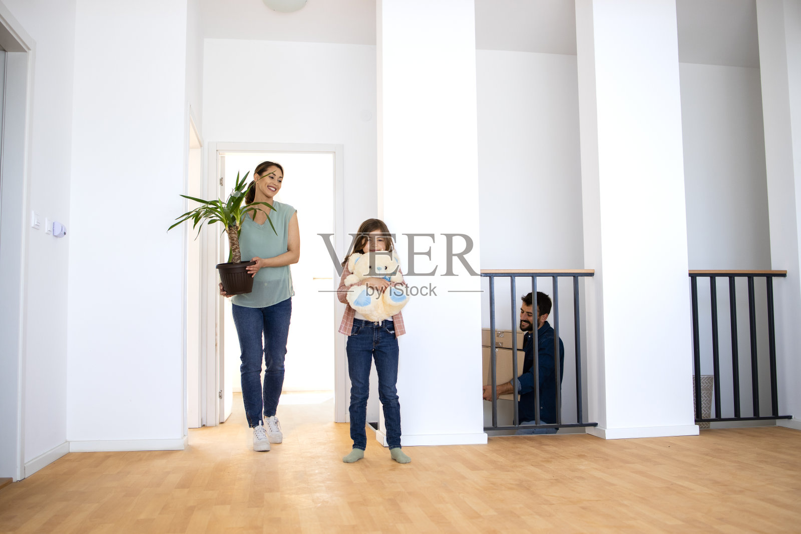 一个年轻的家庭搬着鲜花和箱子搬进了新公寓。照片摄影图片