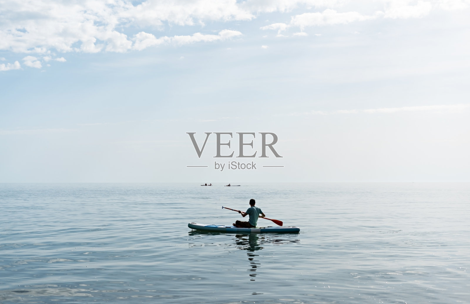 在阳光明媚的夏日，年轻人从后面站在海上划水板上照片摄影图片