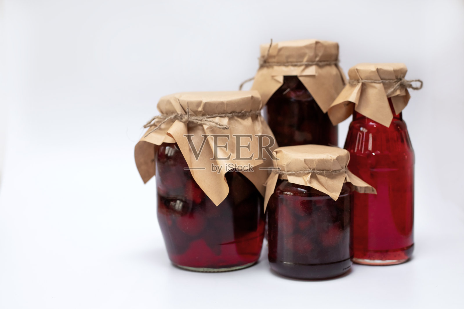 不同形状的草莓糖浆和果酱罐子放在一个白色的盘子里。照片摄影图片