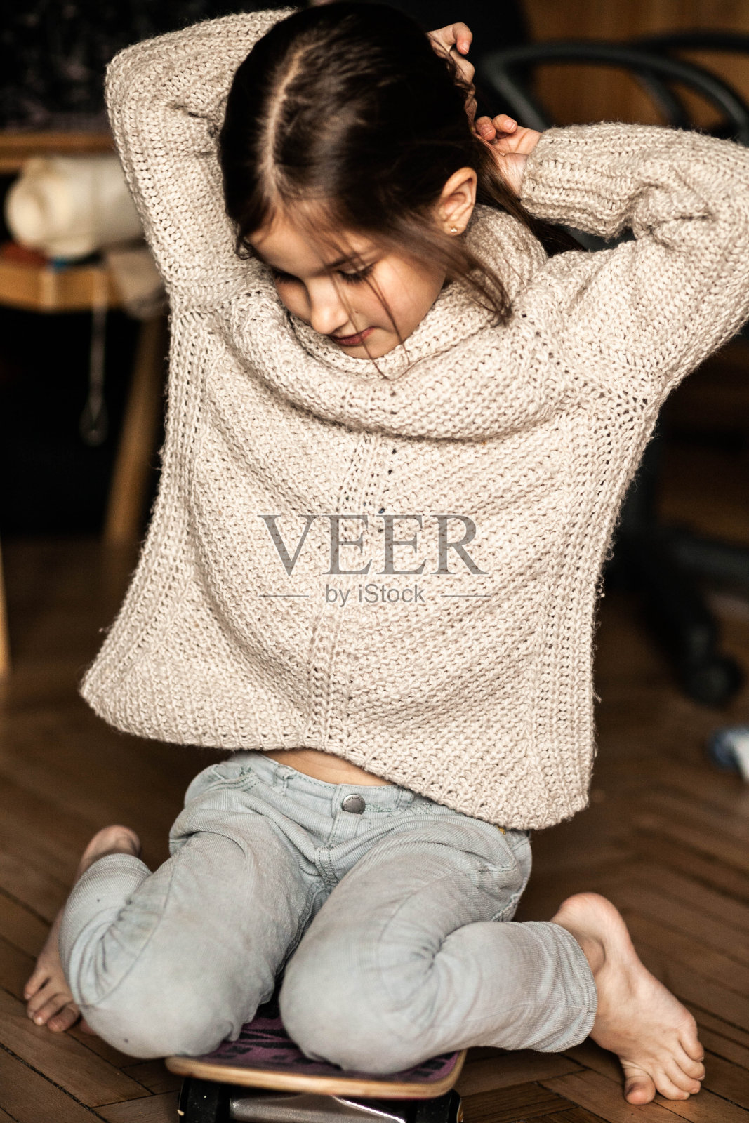 一个6岁的黑头发女孩在家里穿着毛衣，踩着滑板，拉直头发，长发，特写，情绪，蓝色的眼睛，在家里室内，彩色照片，照片为股票照片摄影图片