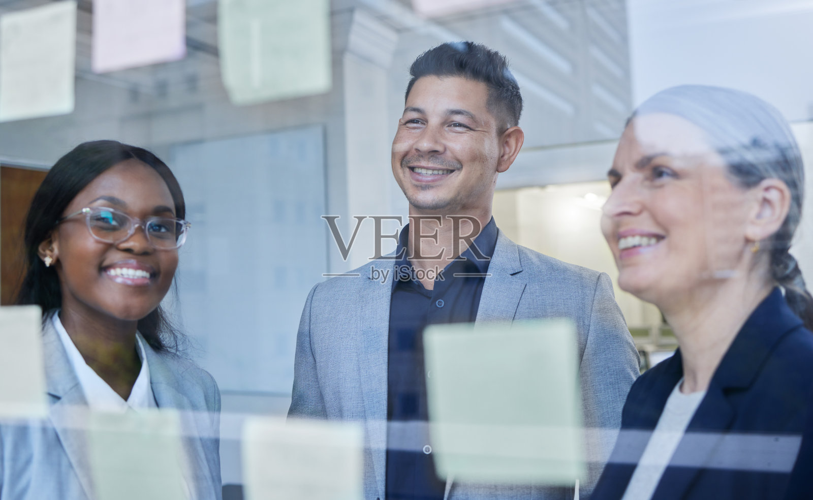这张照片拍摄的是一群商人在办公室的玻璃墙上用笔记进行头脑风暴照片摄影图片
