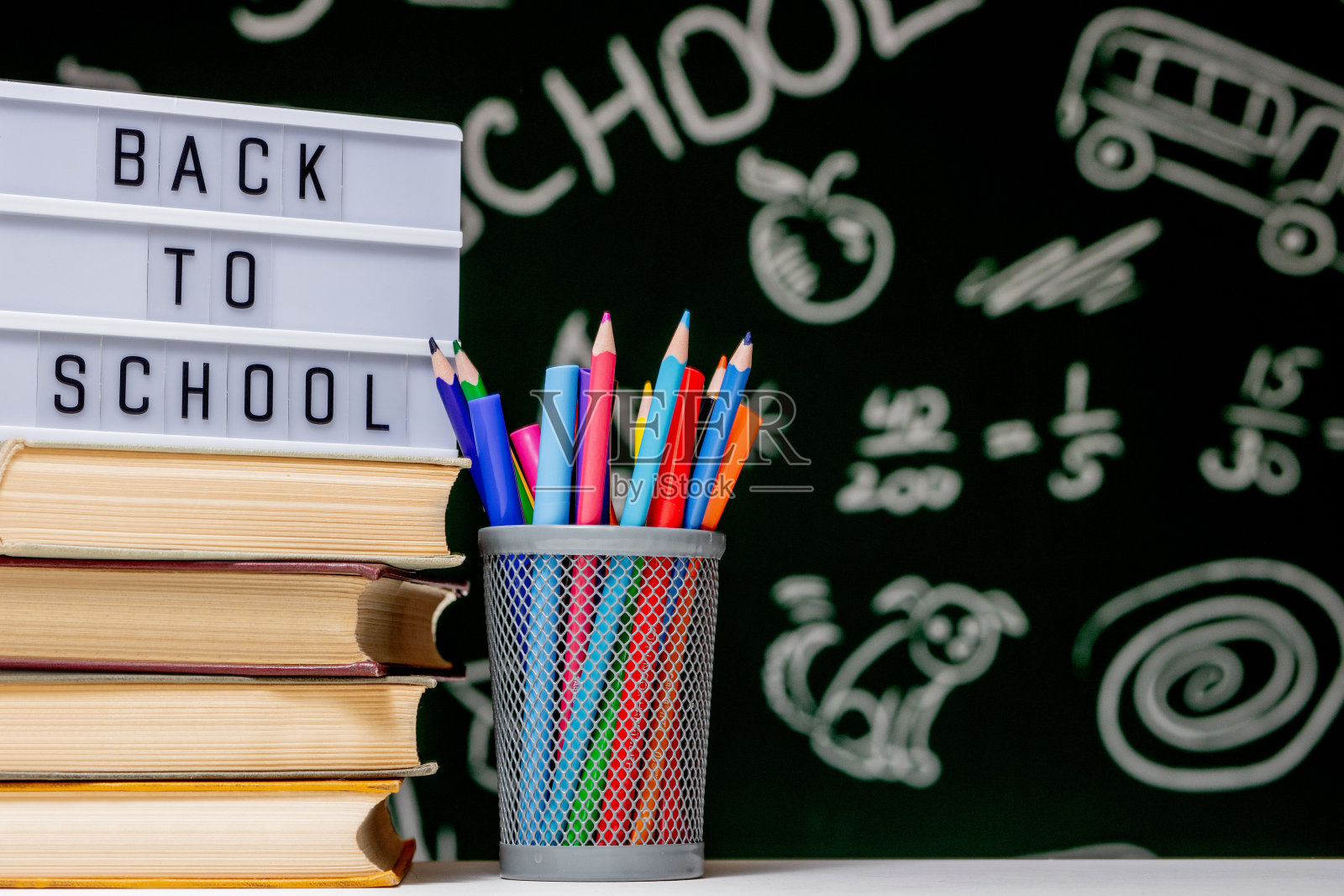 回到学校背景与书籍，铅笔和地球灯在白色的桌子上，在绿色的黑板背景。照片摄影图片