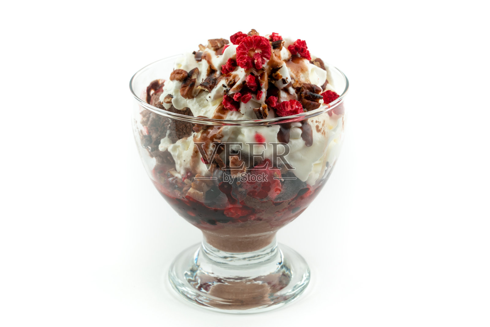 巧克力冰淇淋与一个奶油，各种坚果和冷冻浆果在上面，在一个玻璃杯，孤立在白色的背景。照片摄影图片