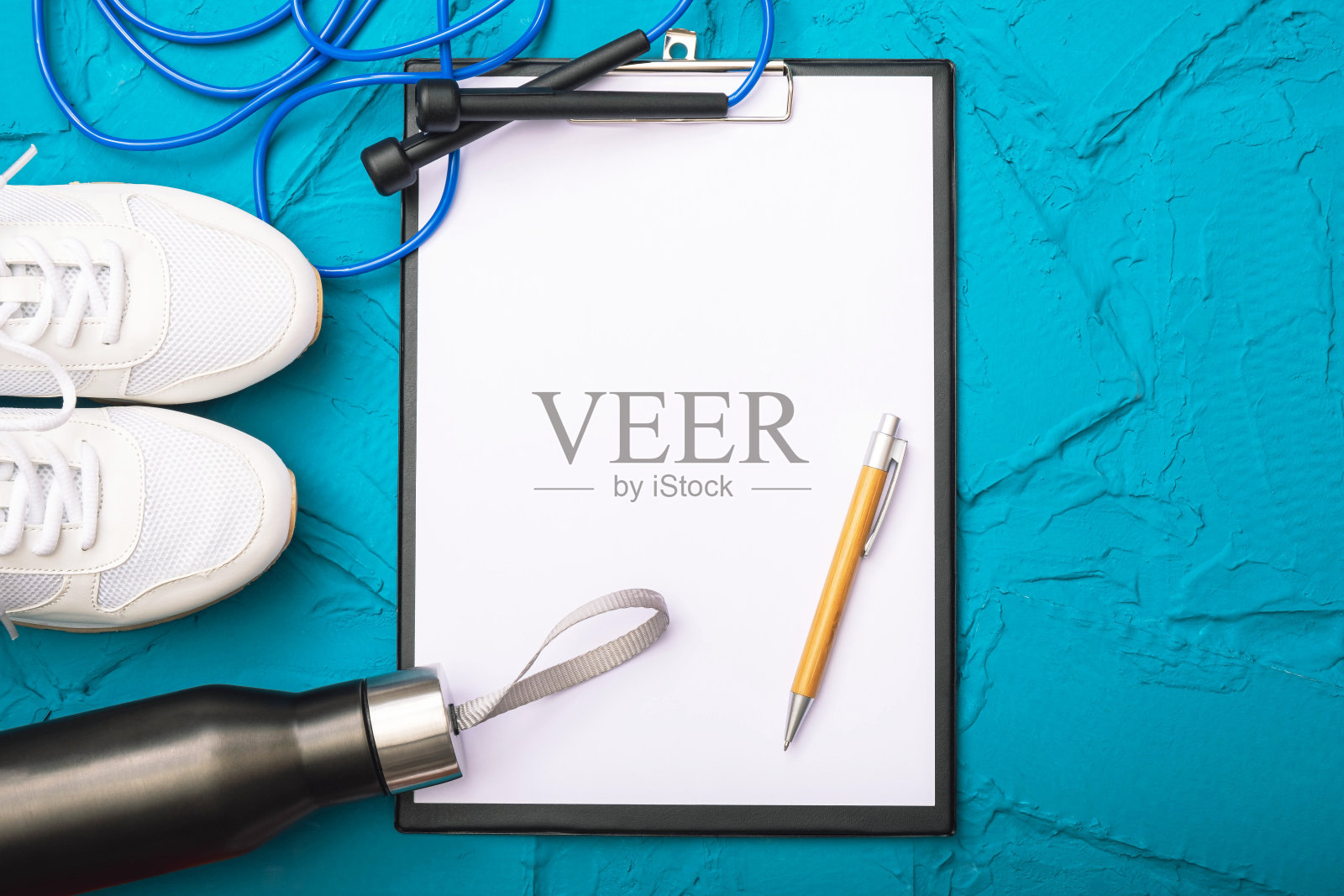 在家健身——瓶子里有水，白色运动鞋和一张有把手的纸，蓝色背景上的跳绳照片摄影图片