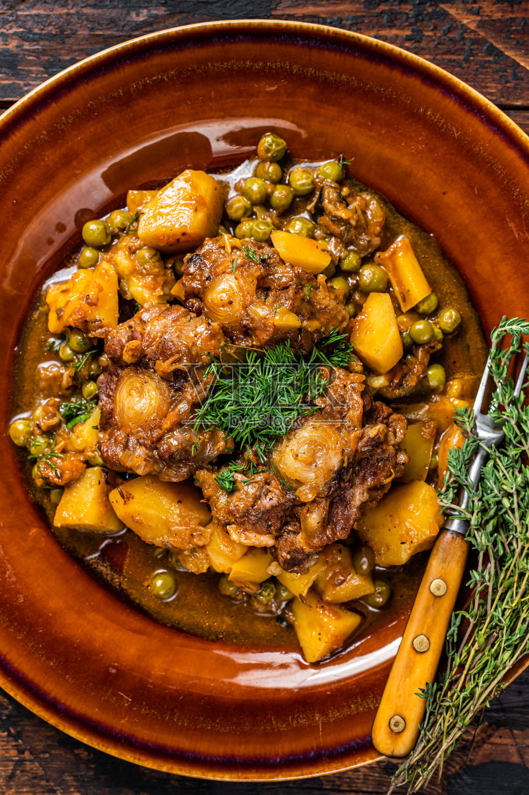 在质朴的盘子里炖蔬菜的牛肉、小牛肉和牛尾。深色木制背景。俯视图照片摄影图片