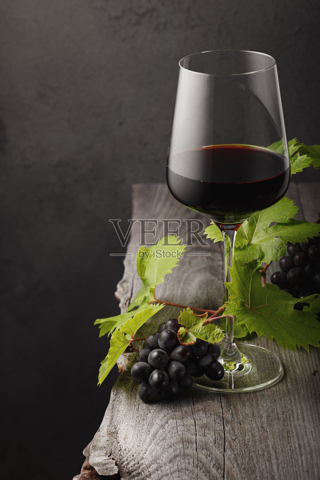 一张旧木桌上放着一杯红酒、葡萄和葡萄叶子。黑暗的背景。照片摄影图片