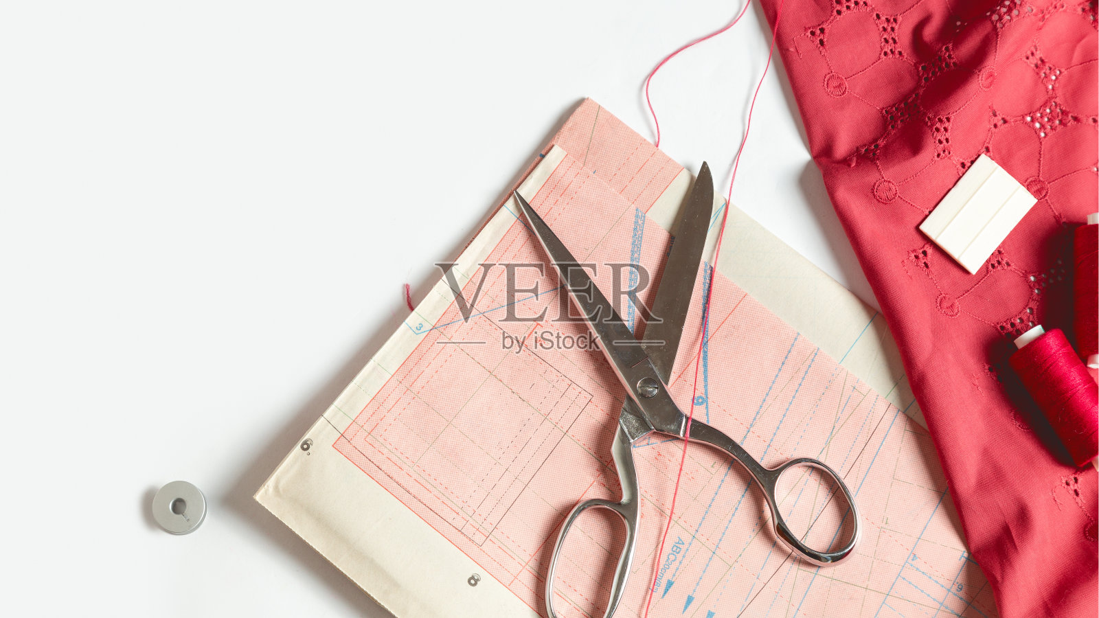 裁缝的桌子上。衣服和缝纫工具的图案。白色背景上的红布、线、线轴、剪刀照片摄影图片