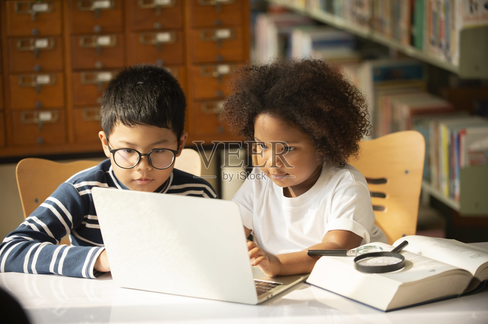一个亚洲男孩和一个可爱的小女孩在图书馆用笔记本电脑一起学习远程教育。照片摄影图片