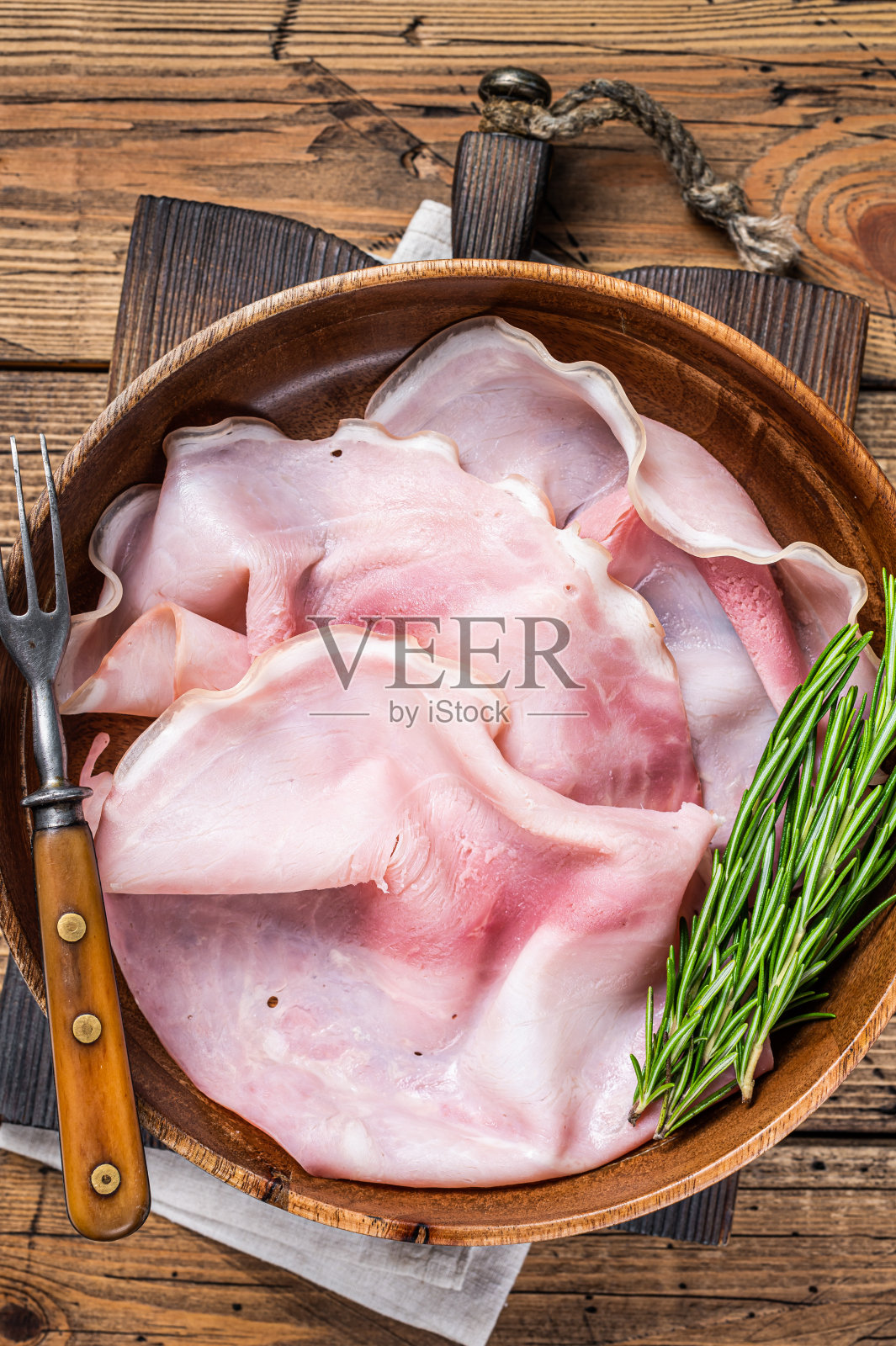 切成薄片的火腿放在木盘子里。木制背景。俯视图照片摄影图片