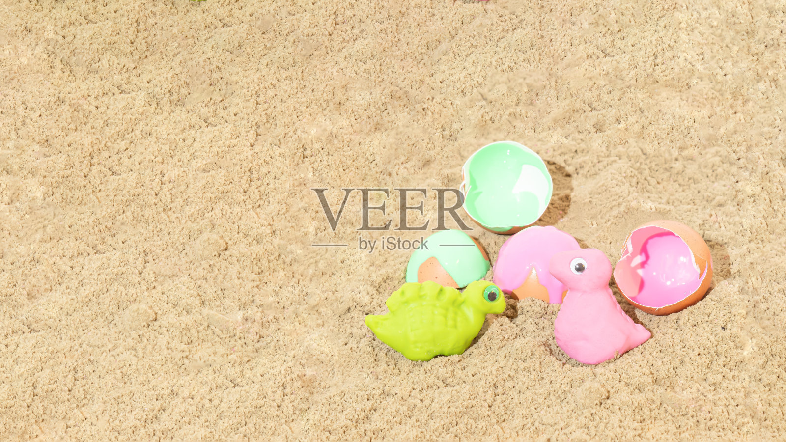 蛋壳旁边用橡皮泥制成的绿色和粉红色的恐龙。沙子的背景。孩子的玩具。最小的概念。照片摄影图片